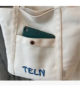 Détail du cabas en toile avec poche à bouton-pression pour tablette et broderie TELN bleue