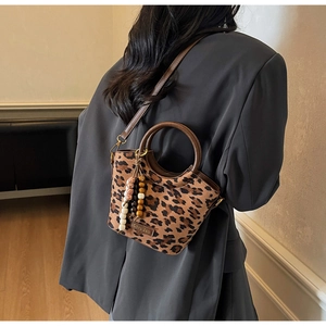 Detail view of leopard print bucket bag with brown handles and bead tassel on gray blazer