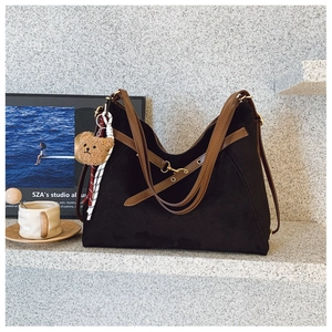 Dettaglio borsa hobo in camoscio nero con manici in pelle marrone e ciondolo a forma di orso