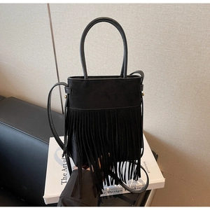 Détail du sac seau noir à franges en daim montrant la texture et la poignée anneau