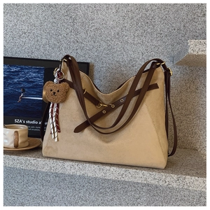 Dettaglio della borsa a spalla in camoscio beige con cinturini marroni e ciondolo a orsetto