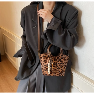 Close-up of leopard print handbag with beaded charm and brown shoulder strap on a model