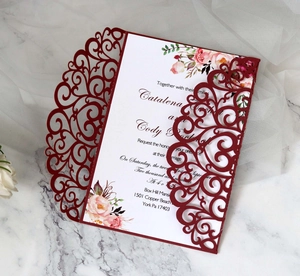 Detailed laser cut burgundy wedding invitation with floral insert on marble background