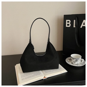 Close-up of black suede underarm bag with smooth zipper and curved minimalist structure