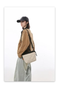 Model wearing beige quilted nylon bucket bag with black straps and orange side tag