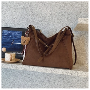 Dettaglio di borsa tote in pelle scamosciata marrone con cinturino e ciondolo a forma di orso