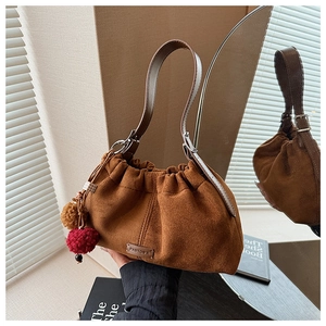Détail du sac seau en daim caramel avec pompon décoratif et plaque de marque dorée