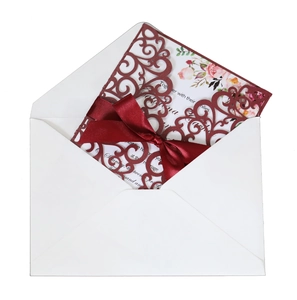 Detail of laser-cut burgundy lace wedding invitation with red silk ribbon and floral insert