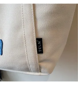 Gros plan du sac cabas en toile beige montrant la texture, les coutures et l'étiquette