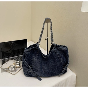 Detail of dark blue denim tote bag with silver chain straps and decorative side buckles