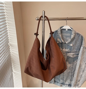 Detail of a brown hobo shoulder bag with a knotted strap and dark spherical charm decoration
