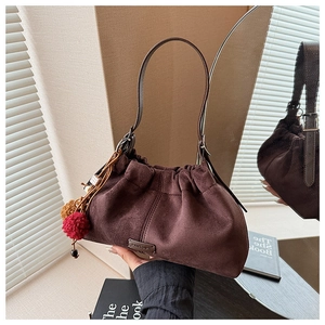 Détail du sac seau en daim marron avec plis à cordon et breloques pompons en peluche