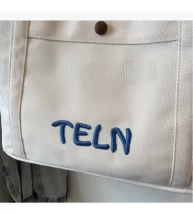 Détail d'un sac cabas en toile avec broderie bleue et bouton décoratif rond
