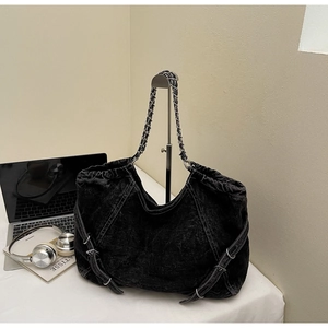 Detail of washed denim bag with metal chain strap and side buckles in a lifestyle setting