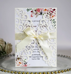 Detail of laser-cut lace wedding invitation with a satin bow and floral insert card