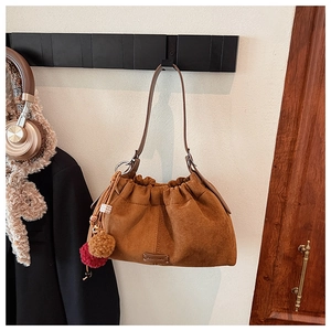 Détail du sac seau en daim marron avec plis coulissants et pendentif pompon décoratif