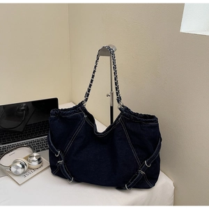 Close-up of denim tote bag with metal chain strap and white contrast stitching details