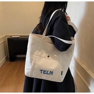 Détail du sac cabas en toile montrant la broderie TELN et la poche avant avec bouton pression