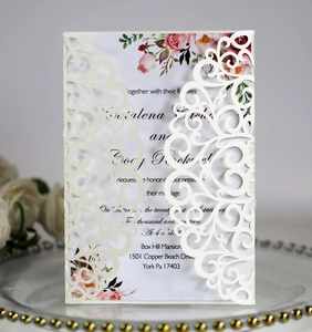 Macro view of laser-cut lace wedding invitation with floral inner card on glass plate