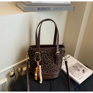 Detailed close-up of leopard print bucket bag with brown straps and colorful bead charm