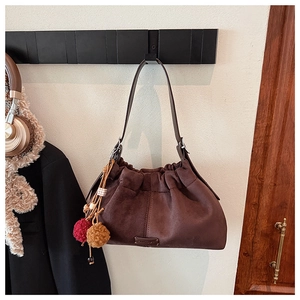 Détail du sac seau en daim marron foncé avec fermeture plissée et breloque pompon bicolore
