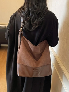 Large brown suede and leather tote bag with adjustable strap worn by a female model
