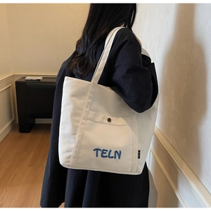 Détail d'un cabas en toile crème avec broderie bleue et bandoulière en gros plan