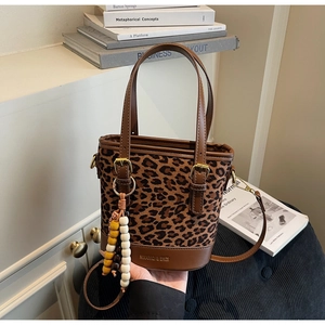 Detail of leopard print bucket bag with brown leather handles and bead charm