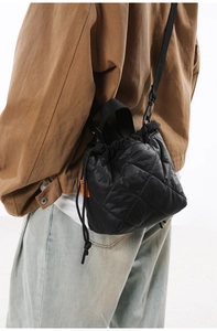 Detail of black quilted nylon bucket bag with drawstring closure and orange woven side label