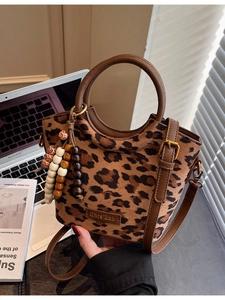 Chic leopard print bucket bag with brown leather handles and a beaded tassel charm