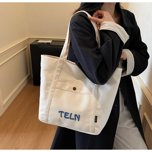 Gros plan du sac fourre-tout en toile blanche avec broderie TELN bleue et poche à pression