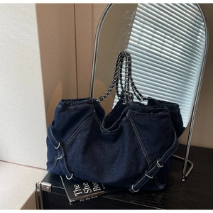 Close-up of blue denim tote bag featuring leather-woven metal chain straps and hardware