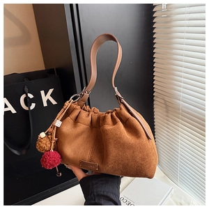 Détail du sac seau en daim marron avec poignée en cuir et pompon décoratif élégant