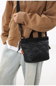 Detail of black quilted crossbody bag with orange brand tag and nylon strap textures