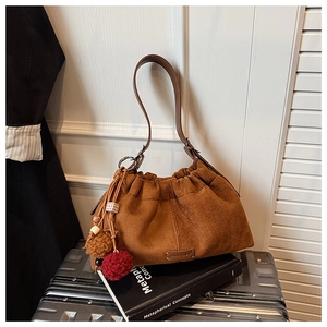 Détail du sac seau en daim marron avec plis élégants et breloques en boules de peluche