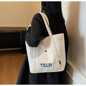 Détail d'un cabas en toile beige avec broderie TELN bleue et poche à bouton en bois