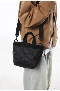 Detail of black quilted shoulder bag with orange label and sleek nylon texture