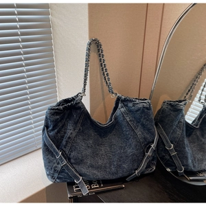 Detail of blue washed denim tote bag featuring woven chain straps and metal side buckles