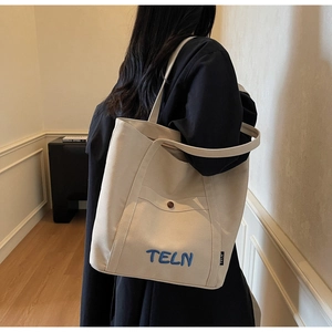 Vue détaillée du sac cabas en toile beige avec broderie bleue et bouton décoratif rouge