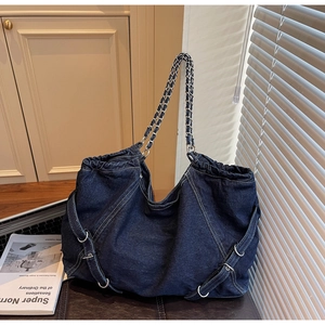Detail of blue denim tote bag featuring silver chain strap and decorative buckle straps