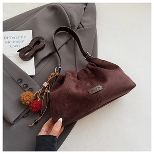 Détail d'un sac seau en daim marron foncé avec breloques ethniques sur un blazer gris