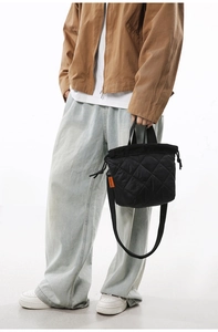 Detail of black quilted bucket bag featuring orange logo tag and drawstring closure