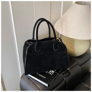Dettaglio borsa a mano in camoscio nero con fibbie dorate in un ambiente minimalista