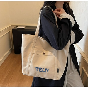 Détail du grand sac cabas en toile beige avec broderie TELN et poche boutonnée devant