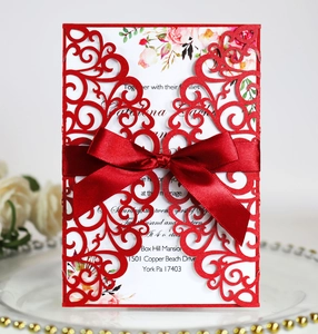 Detailed laser-cut lace pattern on red wedding invitation with elegant satin bow accent