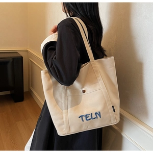 Détail du cabas en toile crème avec broderie TELN bleue et poche à bouton pression
