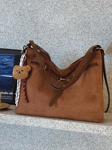 Borsa a spalla in camoscio marrone capiente con ciondolo a forma di orso su sfondo grigio