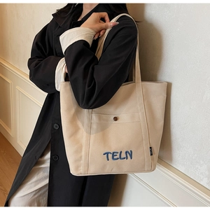Gros plan de la broderie TELN bleu foncé sur le détail d'un sac cabas en toile beige
