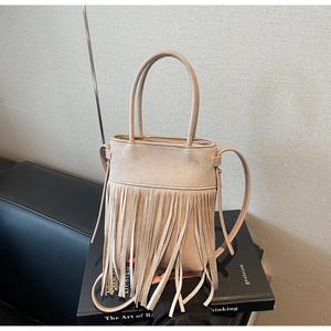 Gros plan du sac à main beige à franges avec poignée cylindrique et fermeture éclair dorée