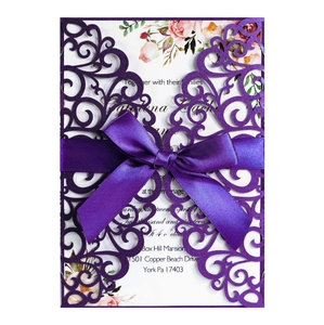 Macro view of purple laser-cut lace wedding invitation with ribbon and floral insert